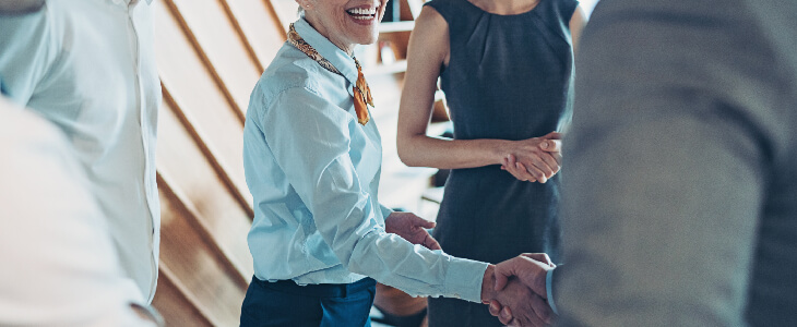 woman shaking hands with a man and happy colleagues around them mergers acquisitions and private equity consulting